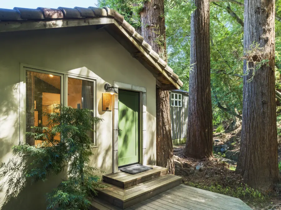 exterior of cottage with a green door, two steps to the door, and a small redwood grove to the right