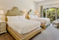Two plush queen beds with fabric headboards, side tables and lamps, side chair, and large glass doors open to treesdouble-queen.jpg