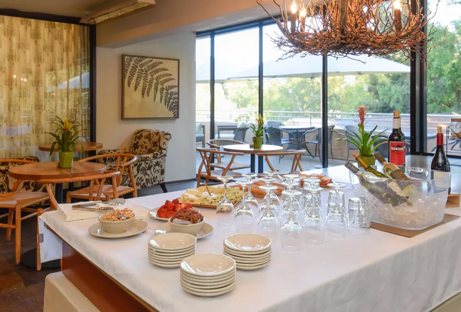 Wine and cheese set up on large table surrounded by tables and chairs with large glass doors leading to patio